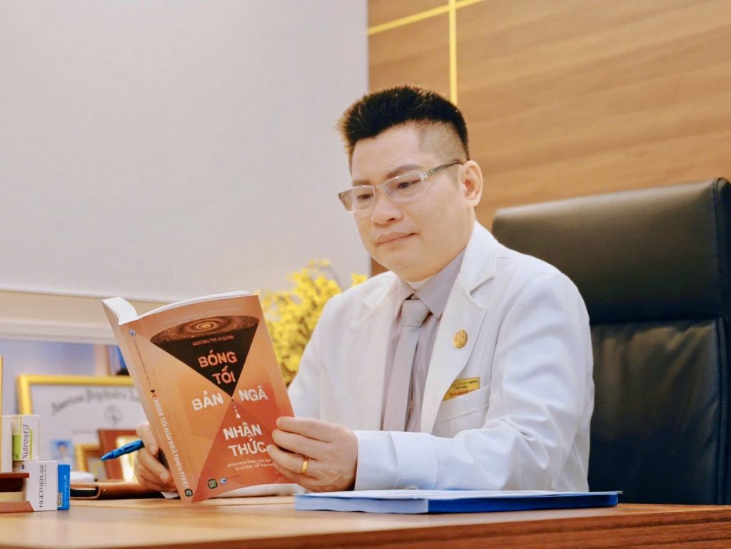 Thạc sĩ, Bác sĩ Đinh Hữu Uân đeo kính, chăm chú đọc sách nghiên cứu tâm lý học tại phòng làm việc.